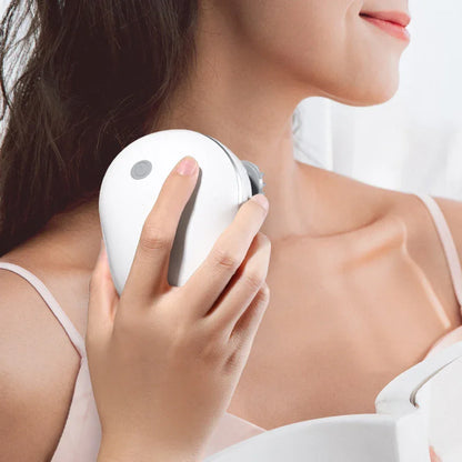 Woman using white handheld massager on shoulder in bright setting for relaxation